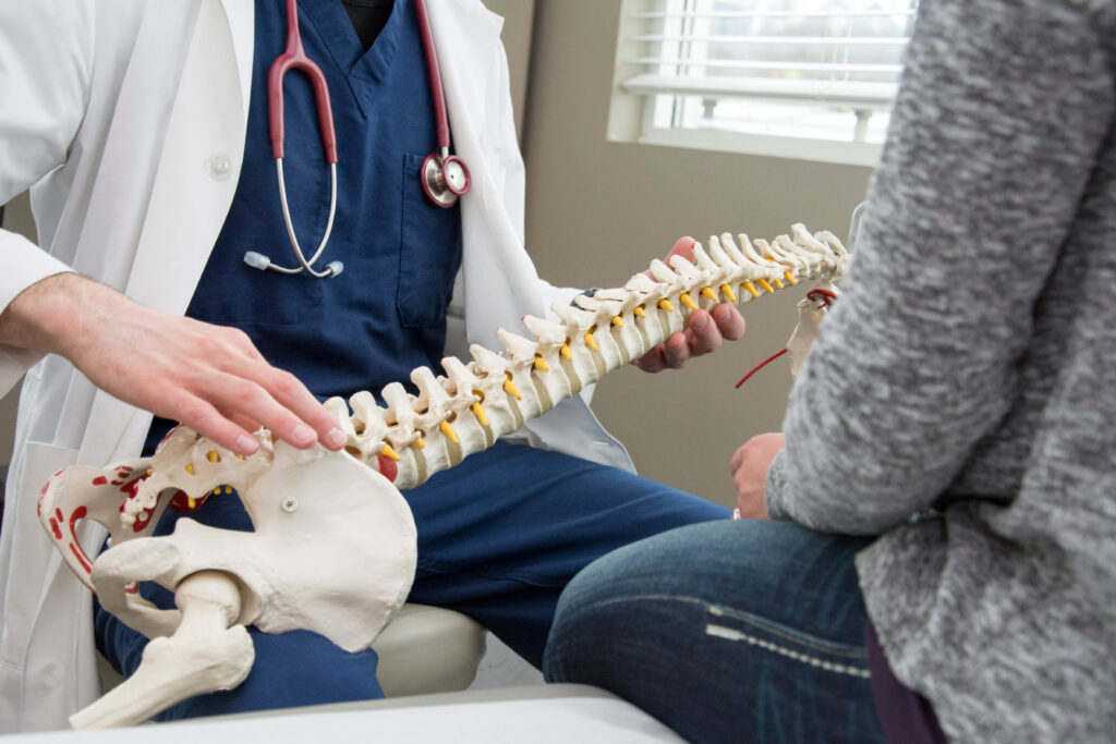 orthopedic surgeon consults with patient while holding a model of the spine.