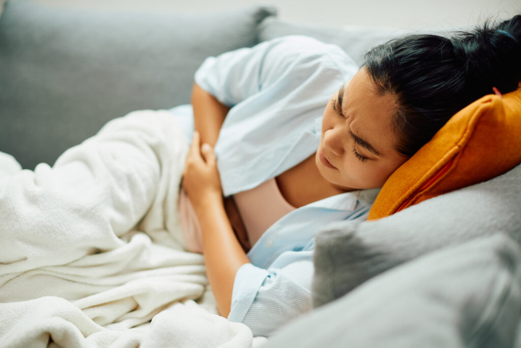 A woman with ulcerative colitis holds her stomach in pain while lying on a sofa