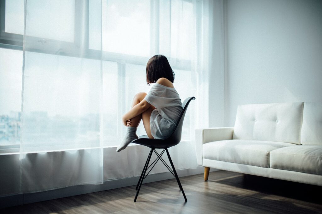 Young woman sitting in a chair facing a window in an apartment