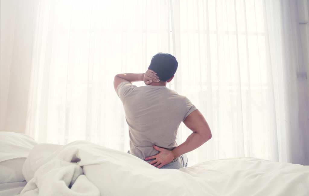 Man with back pain sitting on the edge of a mattress