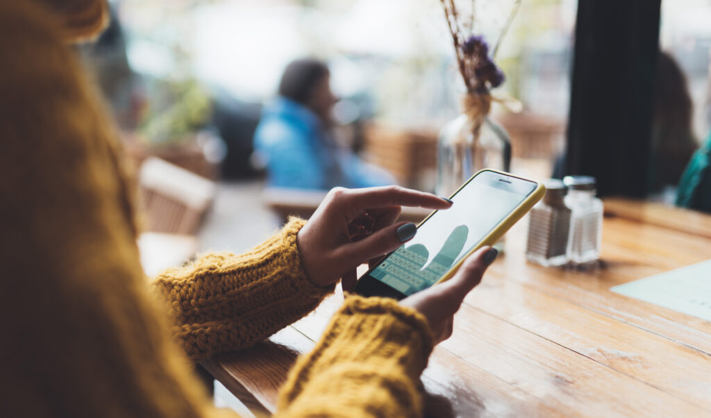 person typing message on smartphone in sunlit cafe.