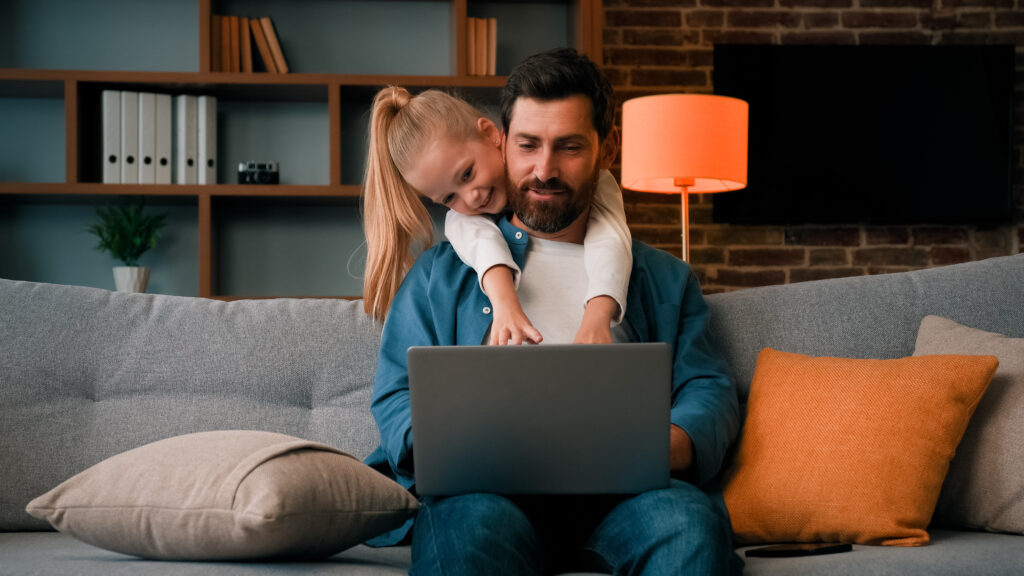 Dad and daughter use laptop together in living room.