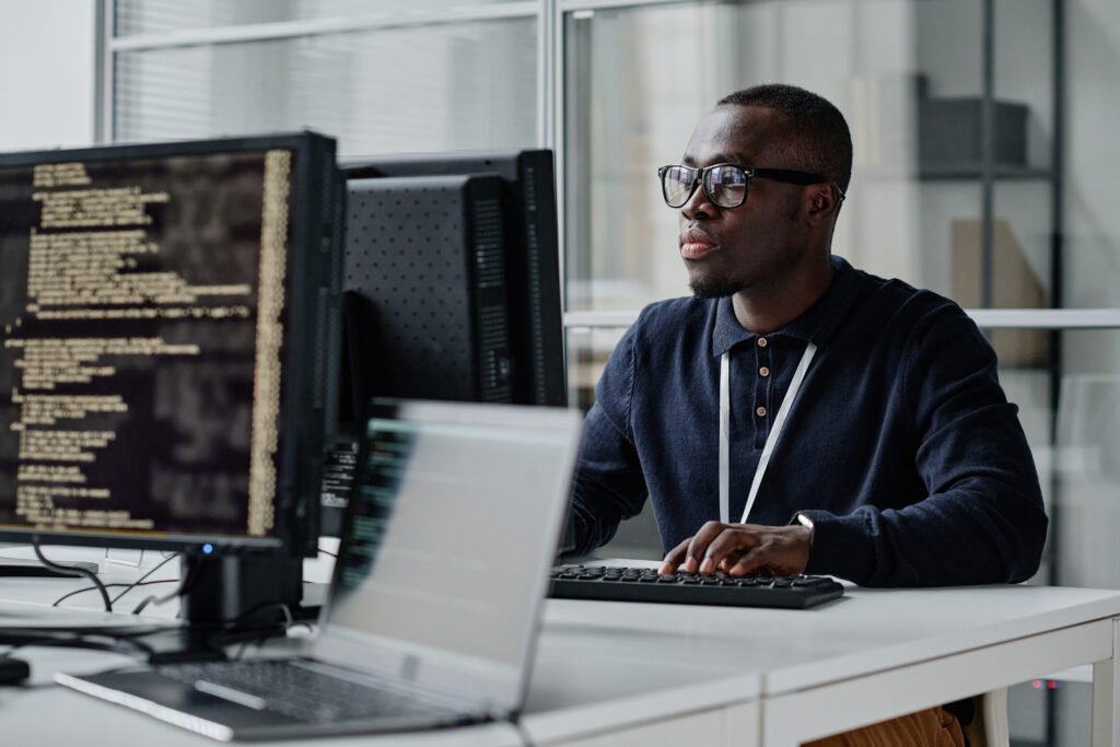  young developer in eyeglasses concentrating on his online work on computer sitting at workplace