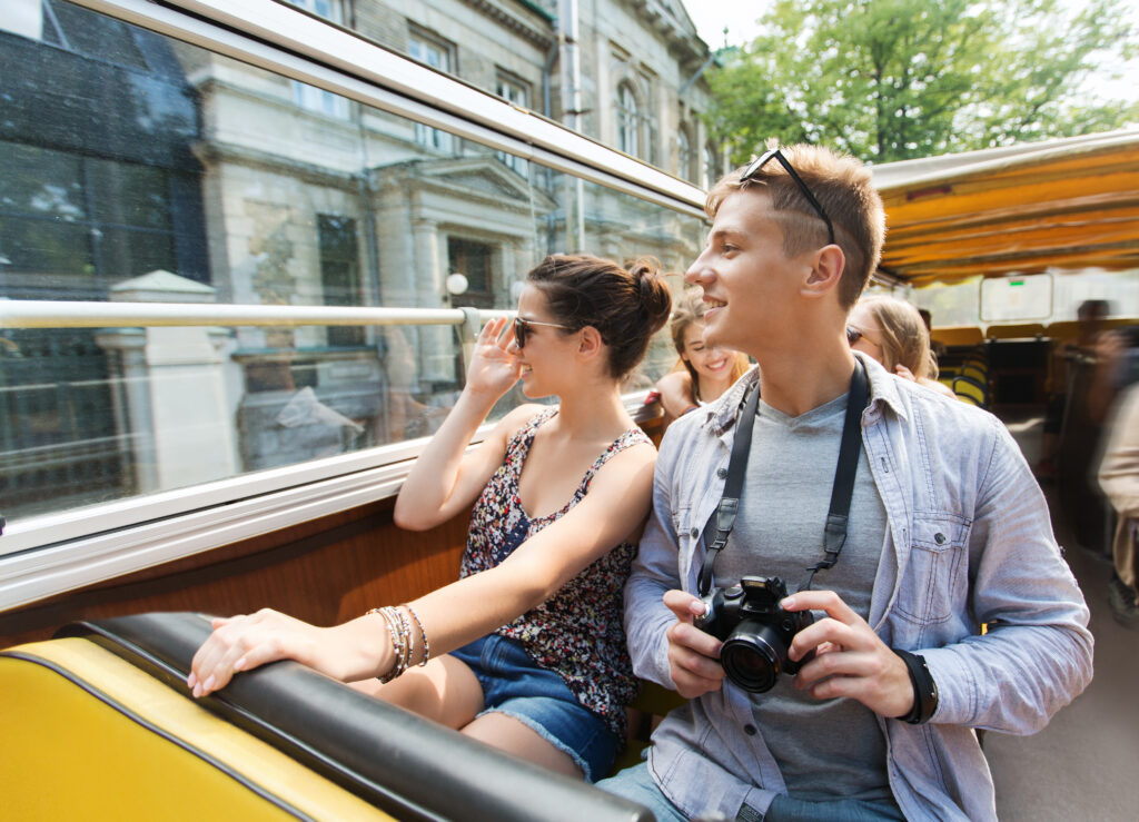 smiling teenage couple with camera traveling by tour bus